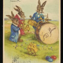 Archiwalna kartka świąteczna, na której stoją na zielonej trawie trzy animowane zające z instrumentami muzycznymi. Na pierwszym planie tańczą dwa żółte kurczaki i trzy kolorowe jajka.