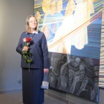 ELżbieta Wasyłyk trzyma różę, stoi na tle pracy.